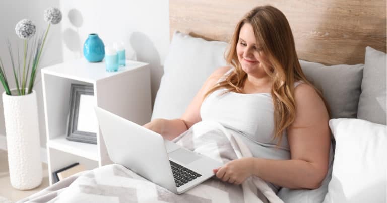 plus size woman on laptop in bed