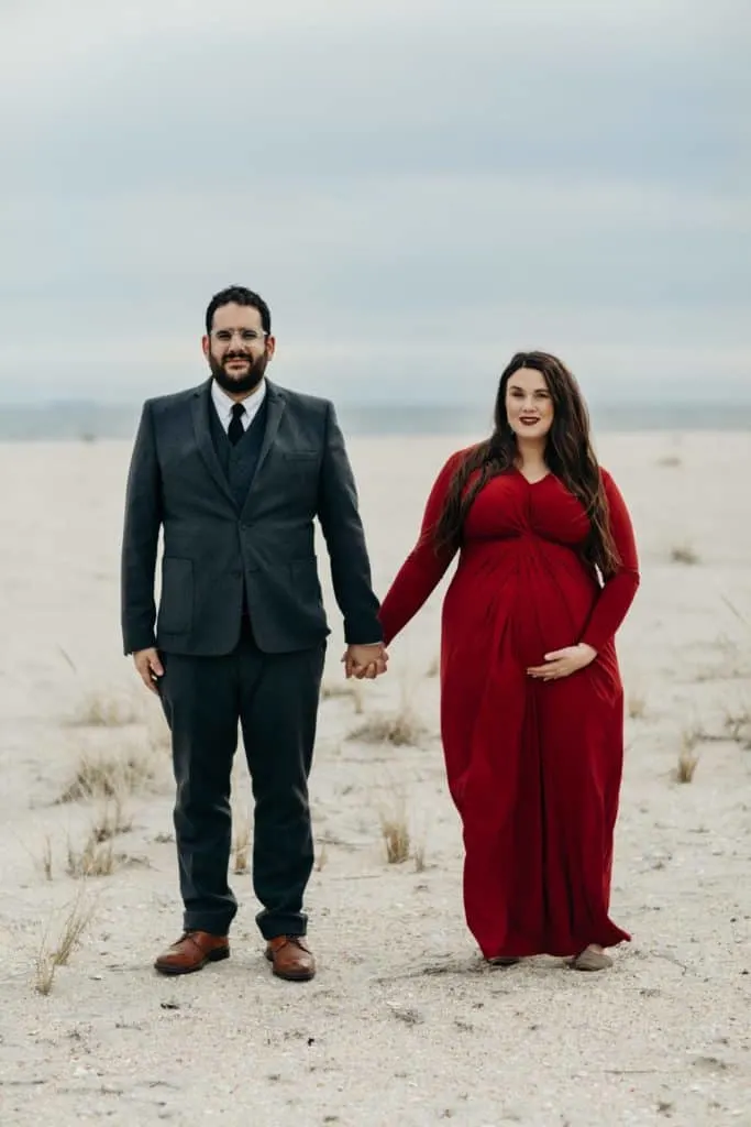 plus size pregnant couple holding hands on the beach. 