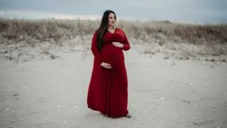 plus size woman in red maternity dress holding her belly on the beach