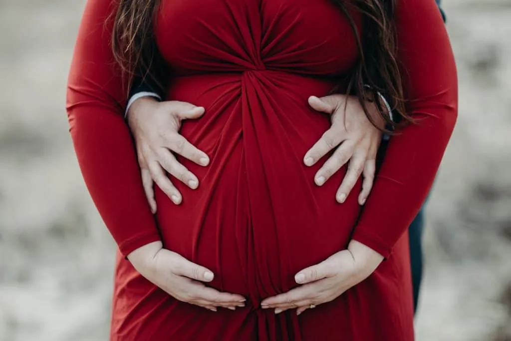 Plus size pregnant belly with husband's hands holding belly. 