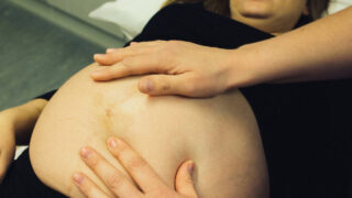 plus size woman receiving care from a midwife touching her belly