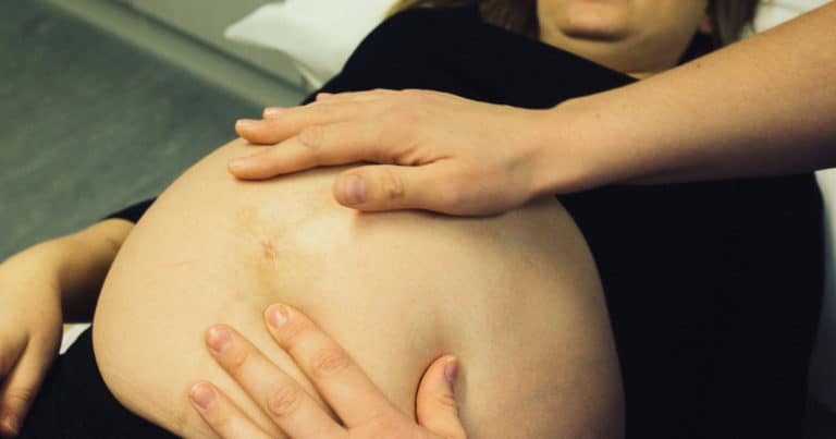 plus size woman receiving care from a midwife touching her belly
