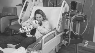 plus size mom in hospital bed kissing newborn baby