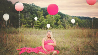 plus size pregnant woman wearing pink dress in a field with pink and white balloons