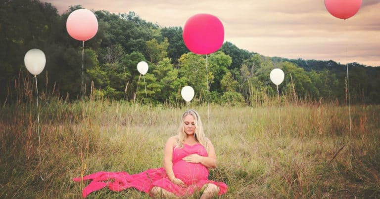 plus size pregnant woman wearing pink dress in a field with pink and white balloons