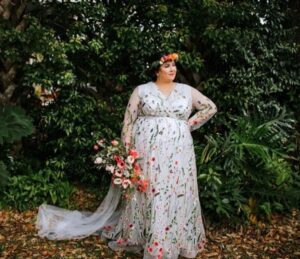 bride standing outside wearing a white plus size wedding dress with embroidered flowers