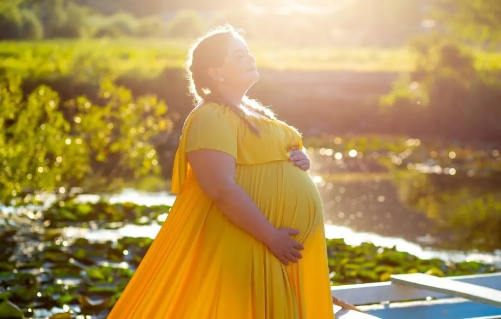 plus size woman wearing a yellow plus size maternity dress from her plus size maternity clothes 