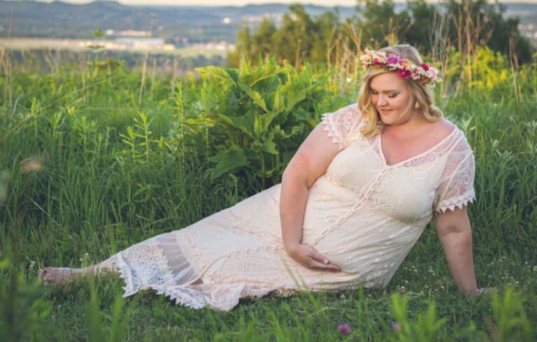 Plus size pregnancy photo laying down in grass wearing a white dress