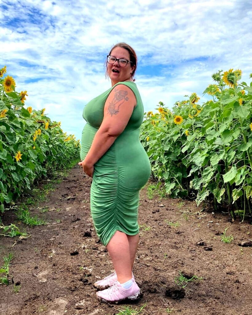 Candid plus size maternity photo in a field with a green dress