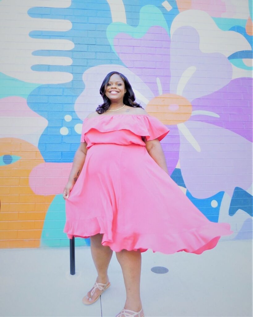 Dress twirl pose maternity pose in a pink maternity dress with colorful background 