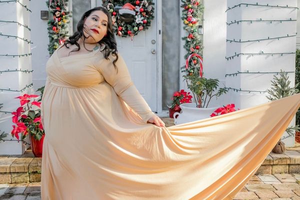 Gown stretch maternity pose of a plus size pregnant woman wearing a gold dress with holiday decorations behind her