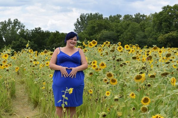 plus size woman doing a heart hands maternity pose in blue maternity dress