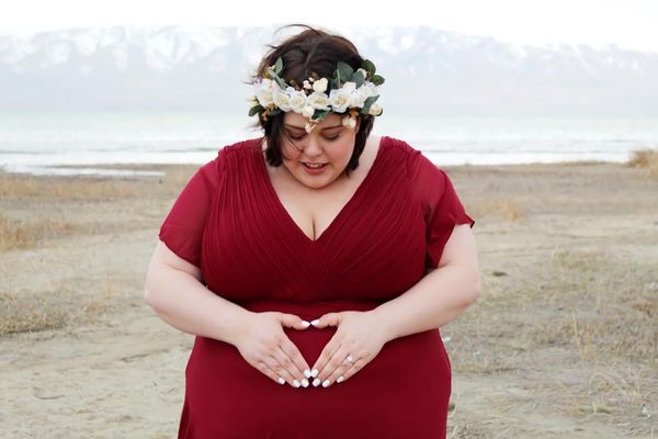 plus size woman doing a heart hands maternity pose in red maternity dress