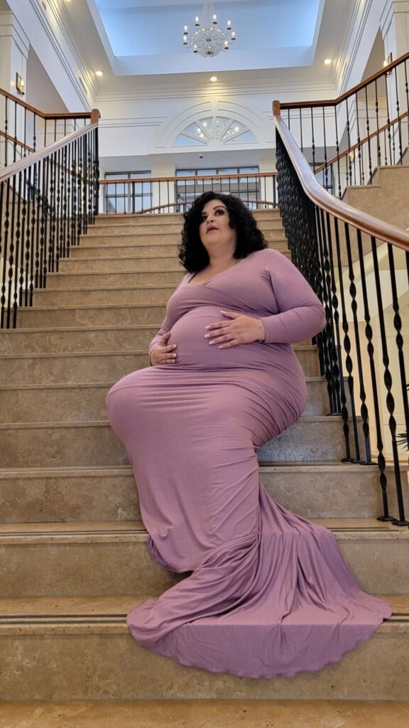 plus size pregnant woman in purple flowing gown seated on steps 