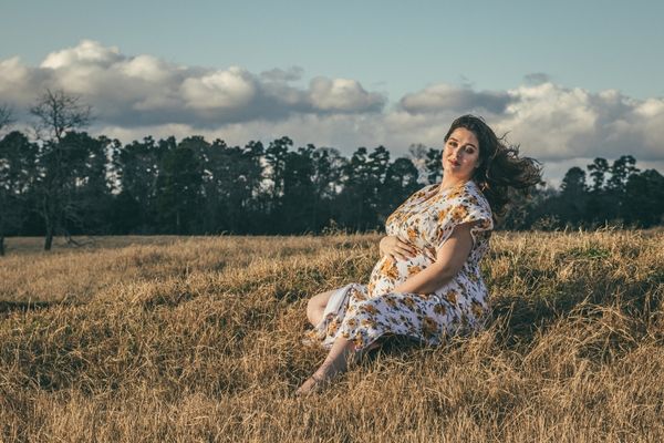 Pregnant woman seated with legs in front plus size maternity pose in the grass