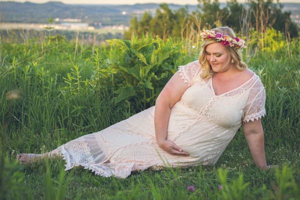 plus size pregnant woman in a side-lying seated plus size maternity pose wearing a white maternity dress with a flower crown