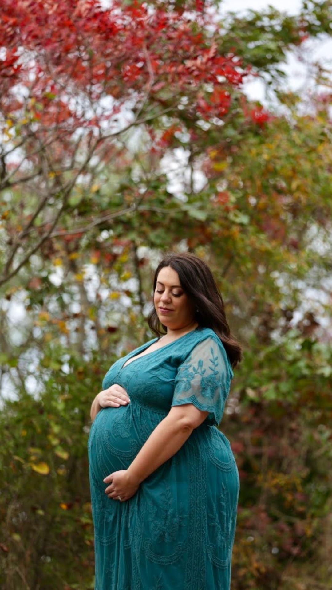 plus size woman in teal dress doing a side maternity pose outdoors