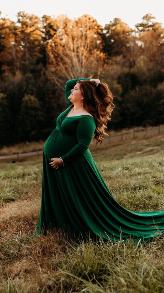 plus size pregnant woman wearing a green maternity gown side pose with one hand in hair