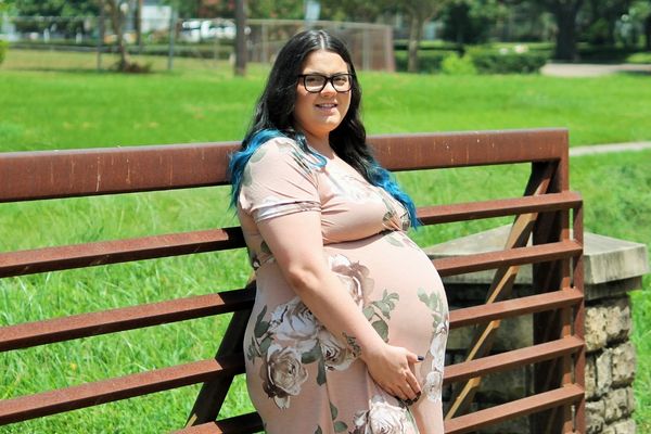 plus size woman in pink floral dress standing with support for a maternity photo shoot
