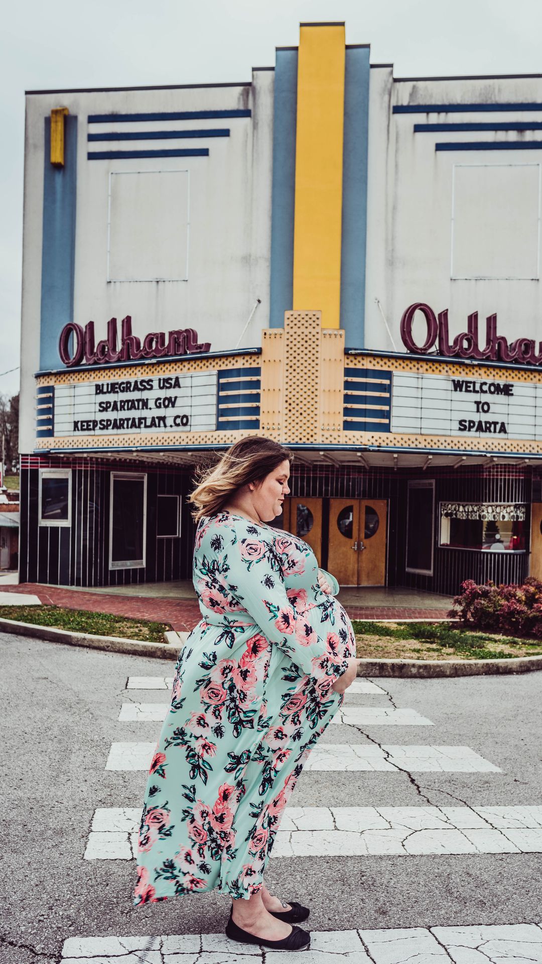 plus size woman taking maternity photos in front of a theater wearing flora dress