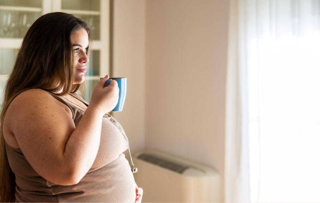 overweight and pregnant woman holding stomach and coffee mug